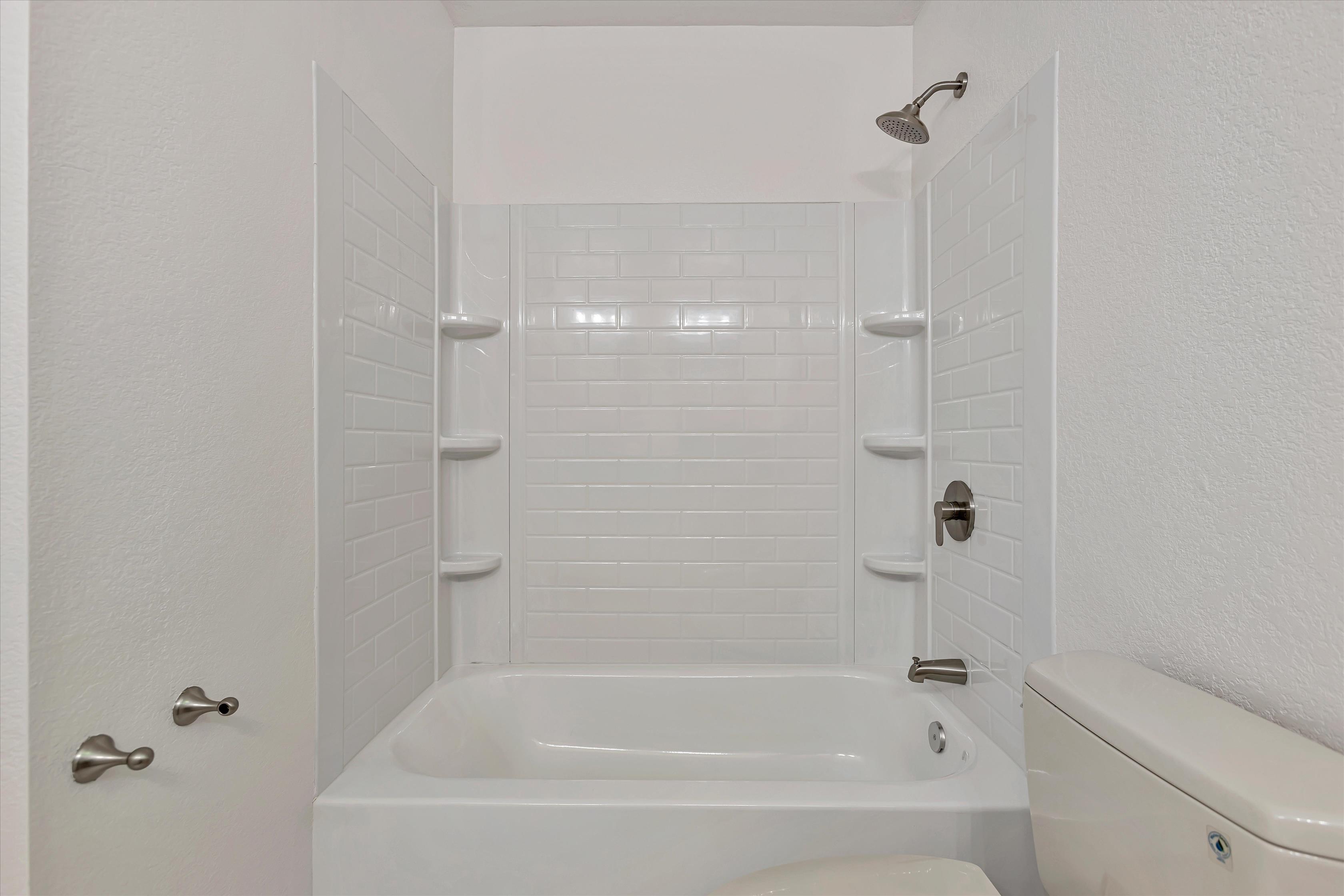 Hall bath tub and shower with subway-tile surround.