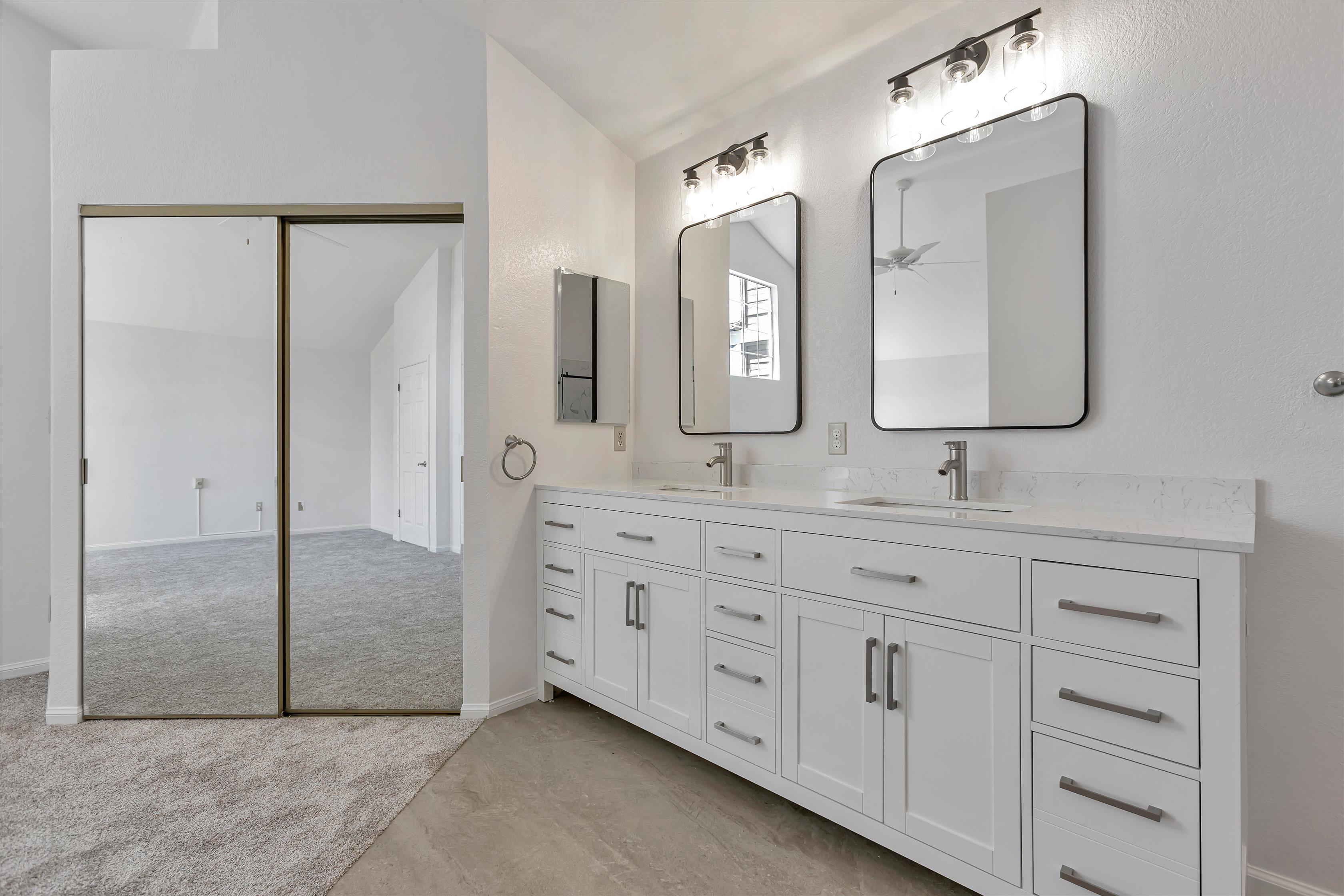 Double vanity with quartz counter and black-framed mirrors.